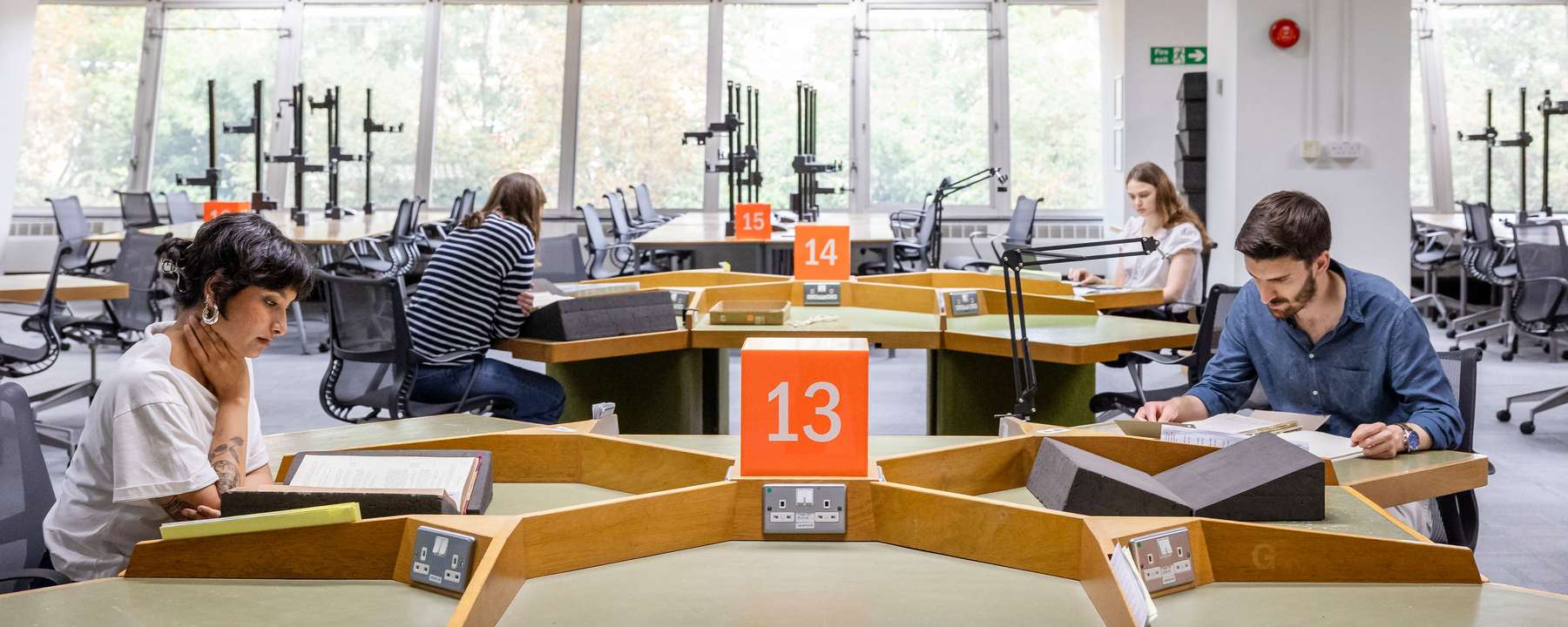 Four visitors sit at tables in a large, open room. Each is looking at a document.