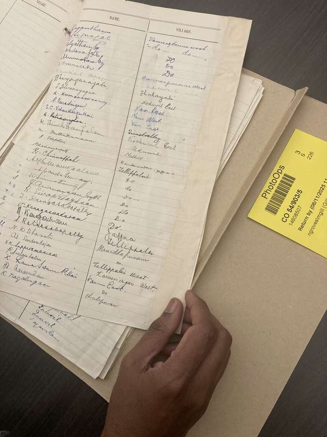 A hand holds the page of a paper document covered with the handwritten names of people and their villages.