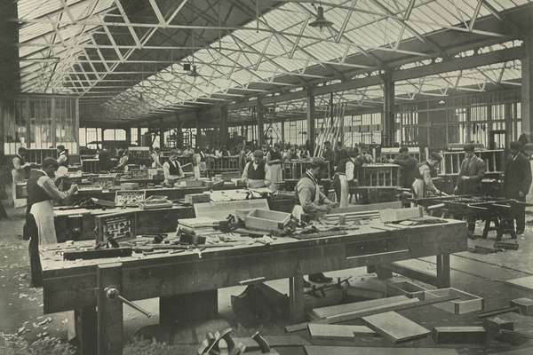 Photograph of workers in a massive sawmill working on heavy machinery.