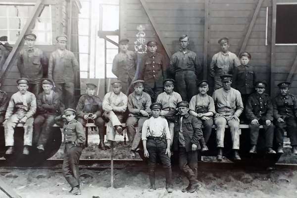 A photograph of a group of 23 men in army uniform, some standing, some sitting, by a train. They are looking at the camera.