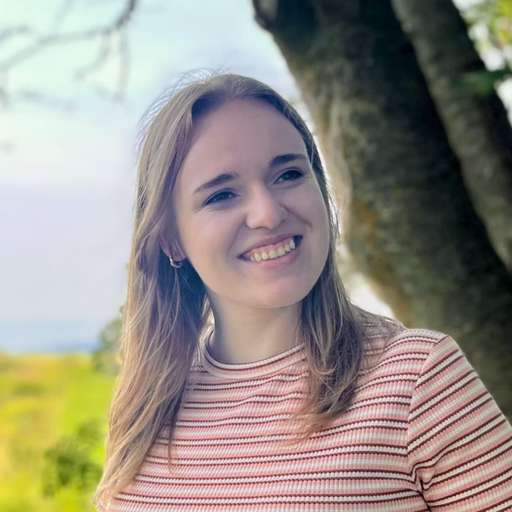 Severine is smiling with her at an angle while looking to the side. She is wearing a pink, orange and white striped shirt