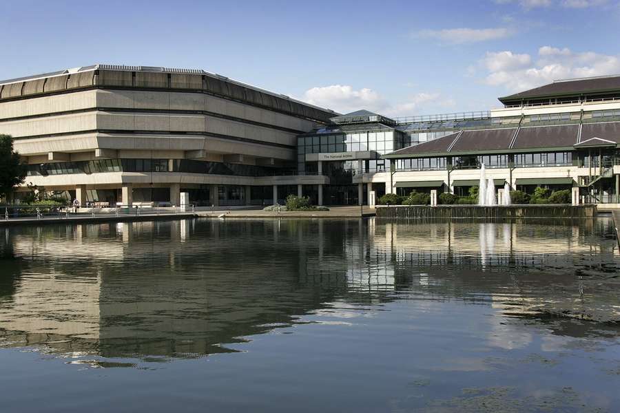 The National Archives building, a brutalist structure joined to a metal and glass one, reflected in the lake below.