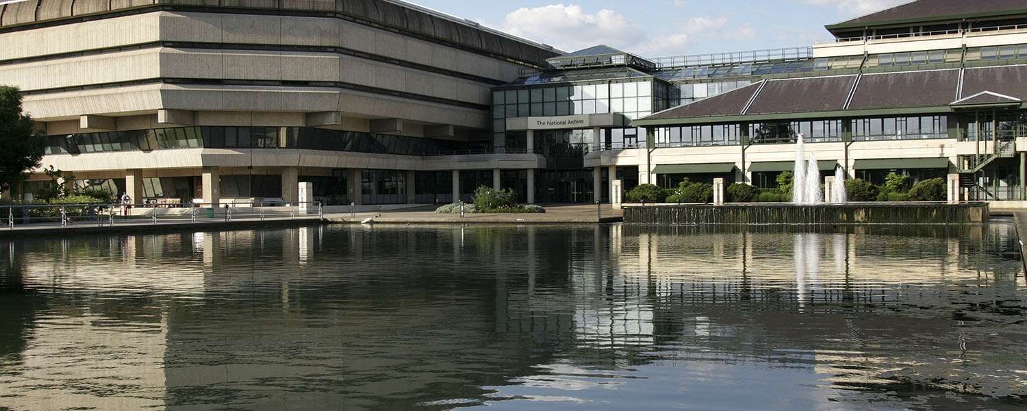 The National Archives building, a brutalist structure joined to a metal and glass one, reflected in the lake below.