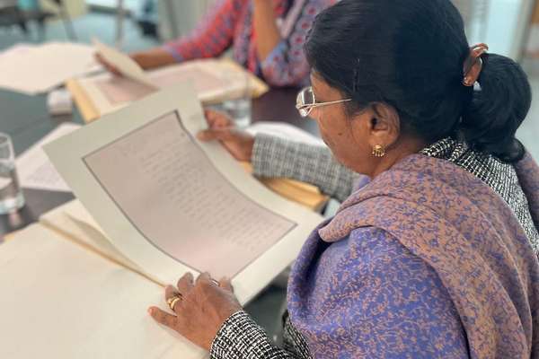 A woman wearing a colourful purple scarf and glasses sits and reads a copy of an archival document.
