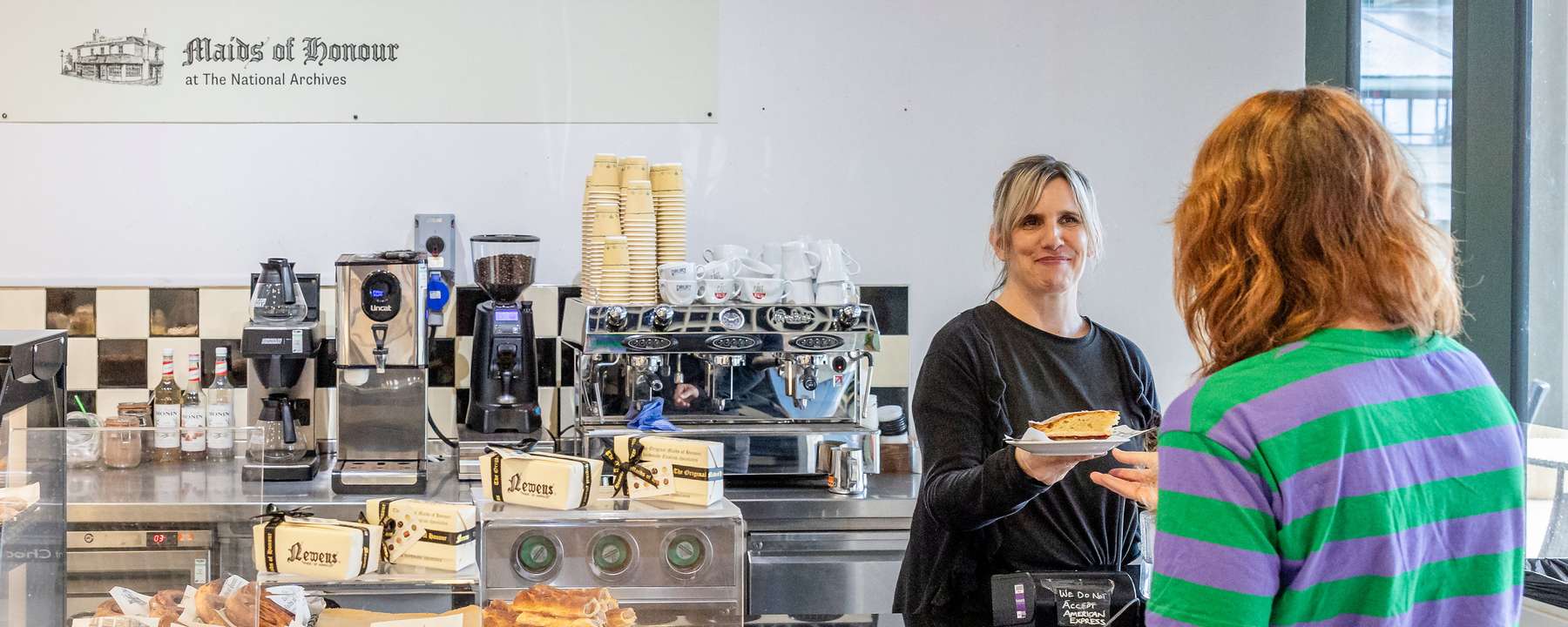 The National Archives coffee bar. A visitor is handed a slice of pie. A coffee machine is visible along with lots of cakes and pastries.