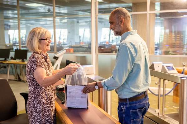 A visitor has their belongings checked by a member of staff. Their belongings are all stored in a clear plastic bag.