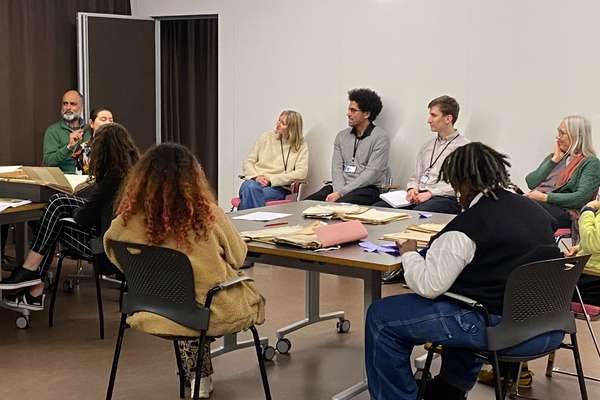 Students and archives staff sit around tables covered with historical documents and books.