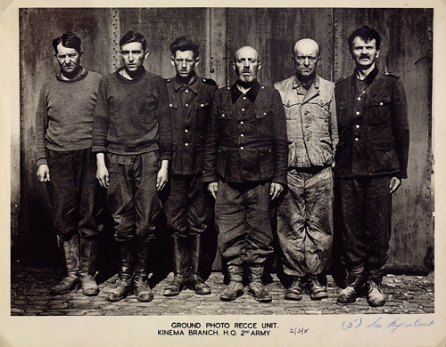 Group photo of six men standing in a row and looking at the camera with serious or sullen expressions.