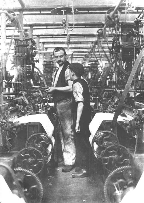 A man talking to a young boy in a factory.