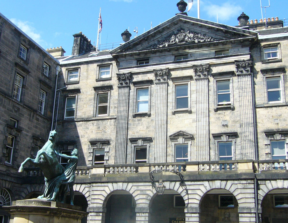 Large ornamental building with a state showing a man with a horse in front.