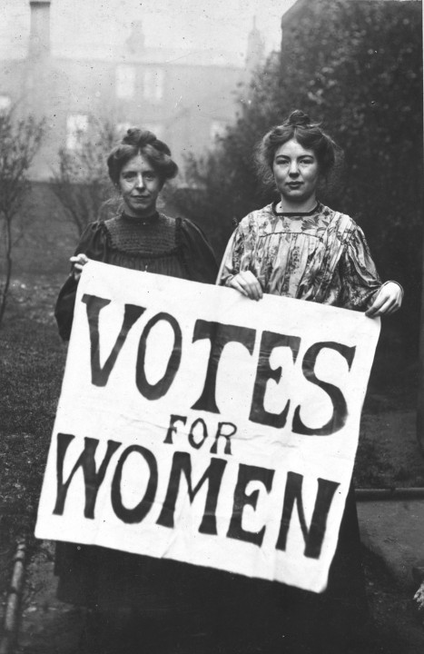 Suffragettes Annie Kenny and Christabel Pankhurst holding up a sign with 'Votes for women' written on it