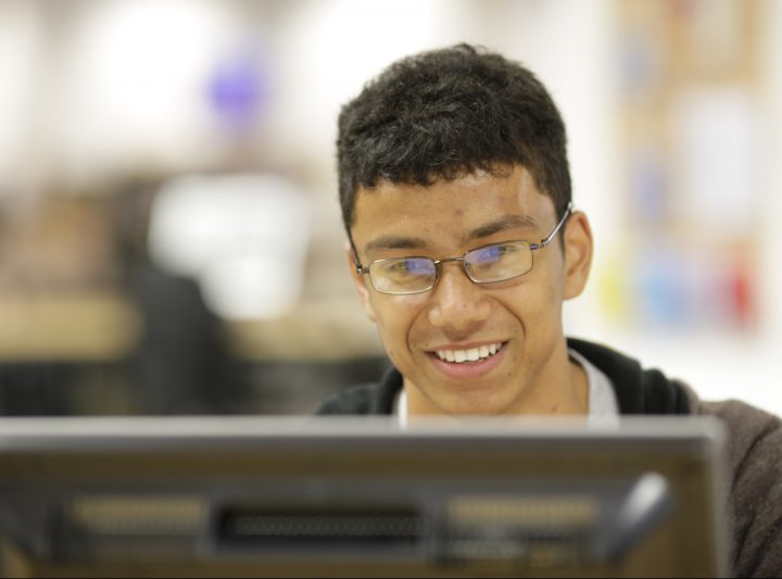 A student smiles while working at his computer