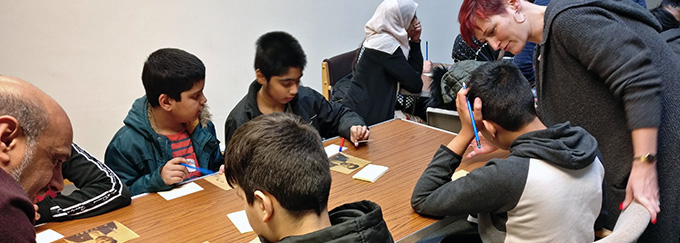 A group of young people sit around a table with pens and archival photographs in front of them.