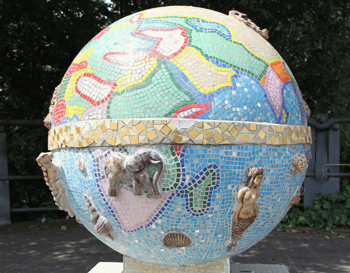 A sculpture consisting of a ceramic globe with a mosaic representing countries, continents, and the equator. Relief sculptures of creatures including an elephant and a mermaid are placed on the globe.