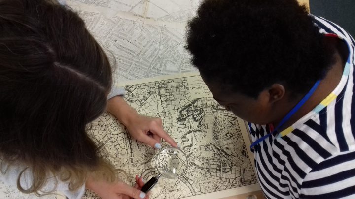Two people hold a magnifying glass up to a map to examine it.