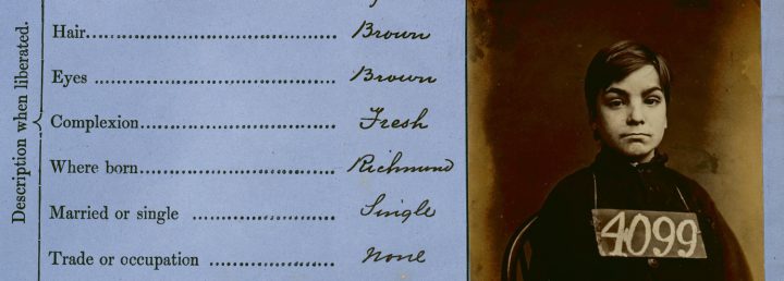 Detail of a document that lists descriptive elements of a person including hair, eyes, and complexion. Next to this list is a sepia toned mugshot of a young boy with the number 4099 on a sign hanging around his neck.