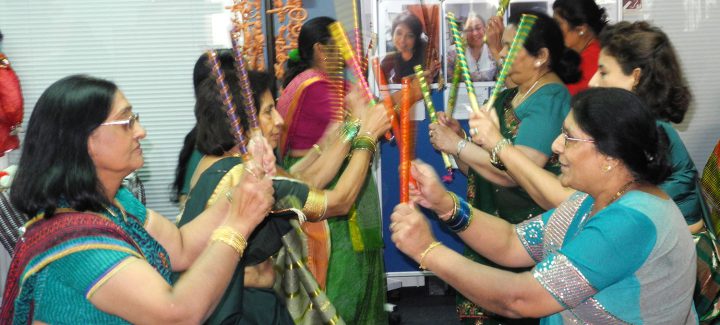 Women in sarees doing a dance using dandiya sticks.