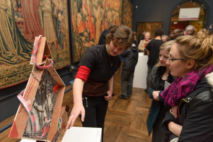 A student gesturing towards a sculpture on a plinth, showing it for some onlookers.