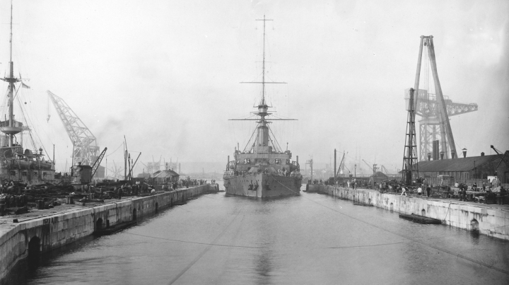 Portsmouth Dockyard, 1914. This is HMS Hindustan entering Dock No.14 (catalogue reference ADM 195/84). Cranes are visible on either side of the canal into which the ship is docking.