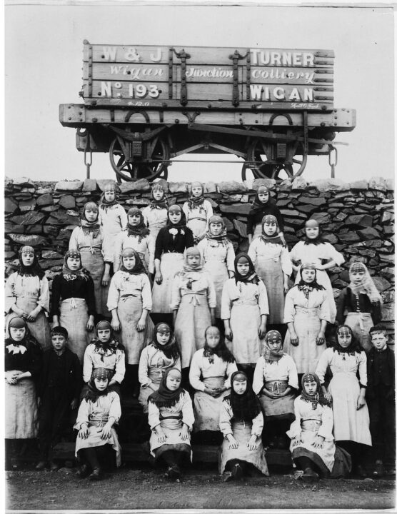 Monochrome photograph of five rows of children standing in front of a wagon with the words W & J Turner Colliery Wigan. They are posed for a group photo.