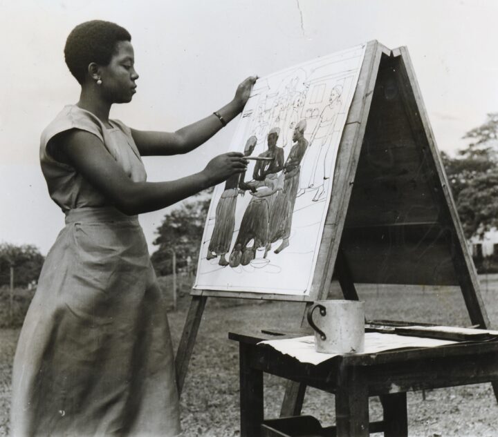 A woman in a dress painting on a canvas outdoors.