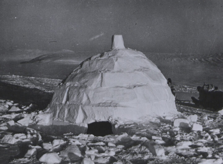 Isolated igloo with short entrance and sleigh parked outside.
