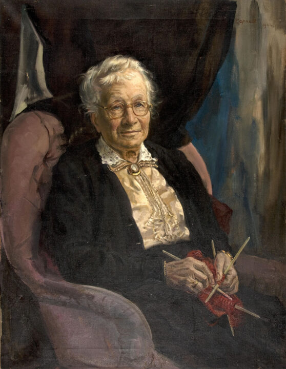 Oil painting of elderly lady, in soft pastel armchair, her red wool knitting rested on her lap. She looks directly at the viewer.