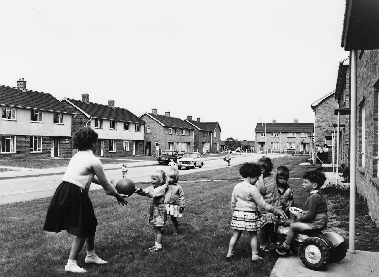 A group of young children play on the grass in front of houses