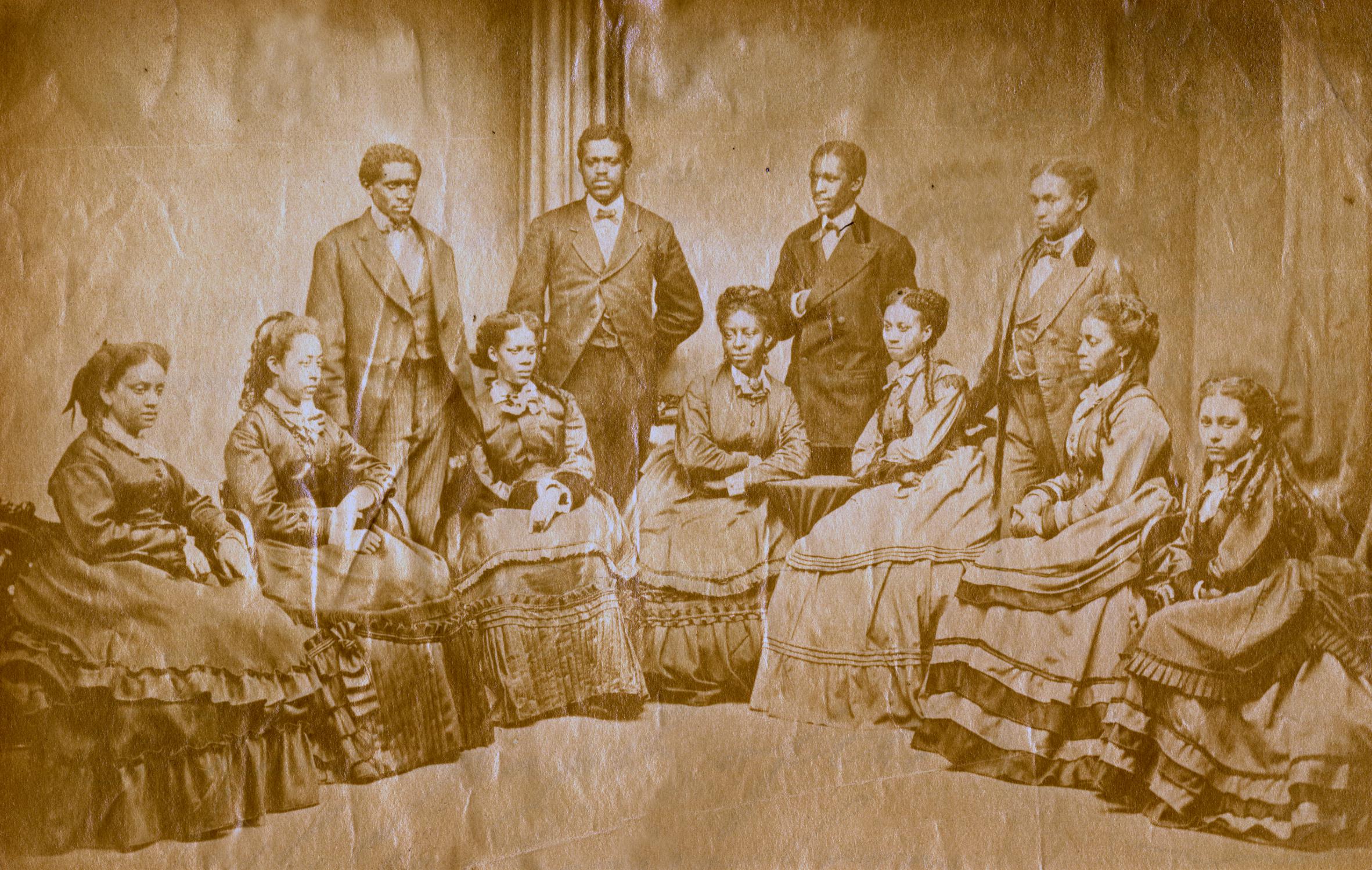 Group photo of eleven African-American men and women. The men wear suits and the women wear dresses with long skirts and sleeves. The men's hair is short and the women's hair is tied up.