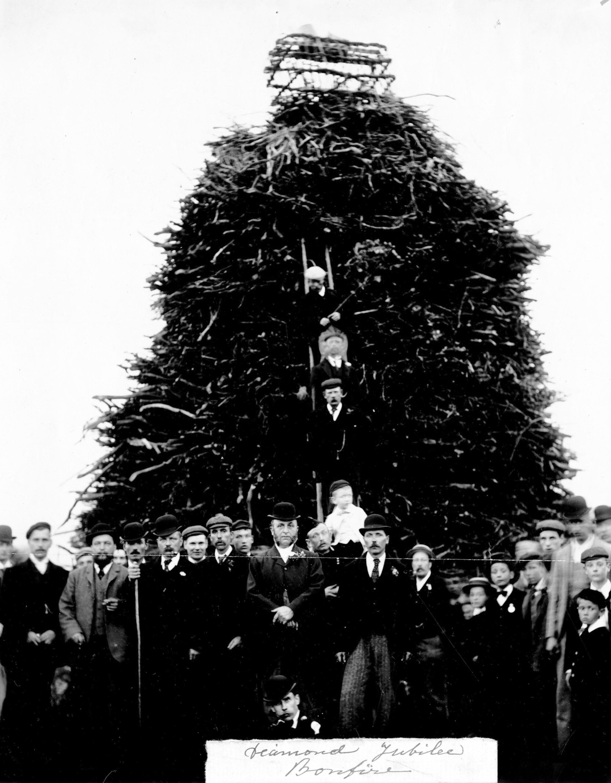 A crowd stands in front of a large bonfire waiting to be lit