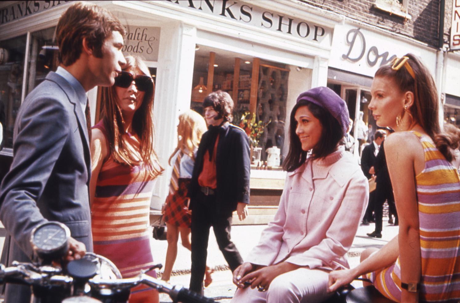 Four young adults in mod fashions sit and talk on Carnaby Street