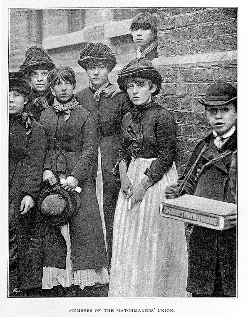 A group of women stand on a street corner looking at the camera. The photo is labelled 'Members of the Matchmakers' Union'.