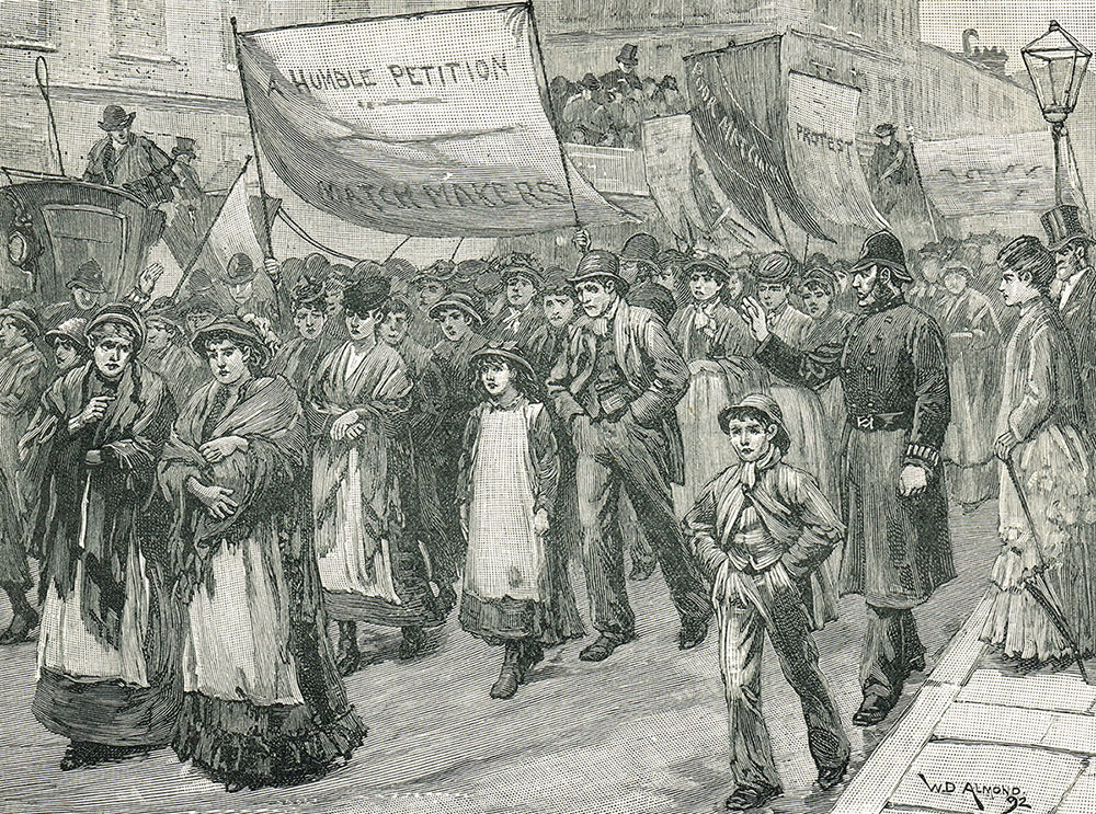 A crowd of people march down the street in a procession holding a big banner saying 'A humble petition - Matchmakers'.