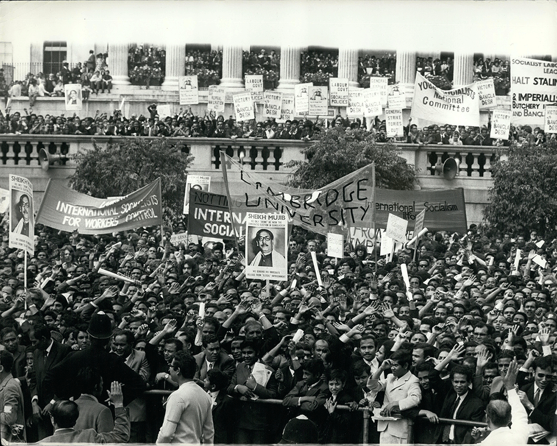 Monochrome photograph of a large crowd of majority South Asian people in Trafalgar Square. A large banner reading 'Cambridge University' is visible, alongside banners for various socialist movements and smaller plaquards featuring Sheikh Mujibur Rahman or 'Victory for Bangladesh'.