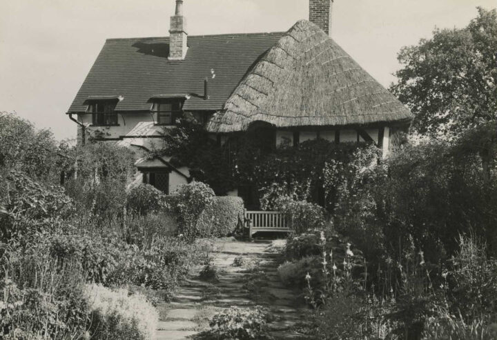 Old but sizeable thatched cottage with a path leading through extensive front garden to the wooden bench outside. 