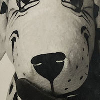 Cropped image. We can see a black upside down triangle surrounded by black dots on a surface of stuffed fabric.