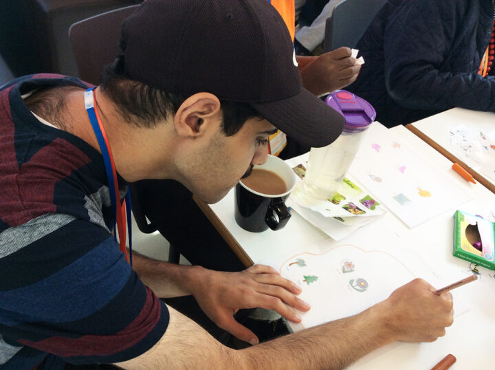 A person sits at a table and draws images of flowers and trees on a large piece of paper.