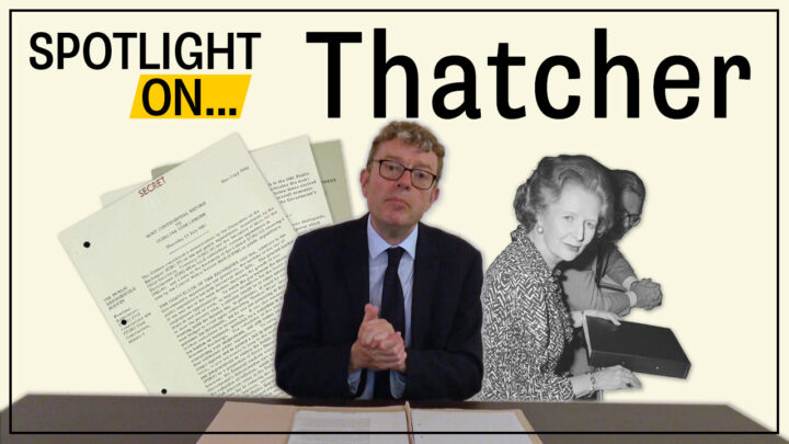 Mark Dunton sits with his hands clasped with an open paper folder on the desk in front of him. A photograph of Margaret Thatcher and Geoffrey Howe and three pages of digitised documents are displayed behind him. 