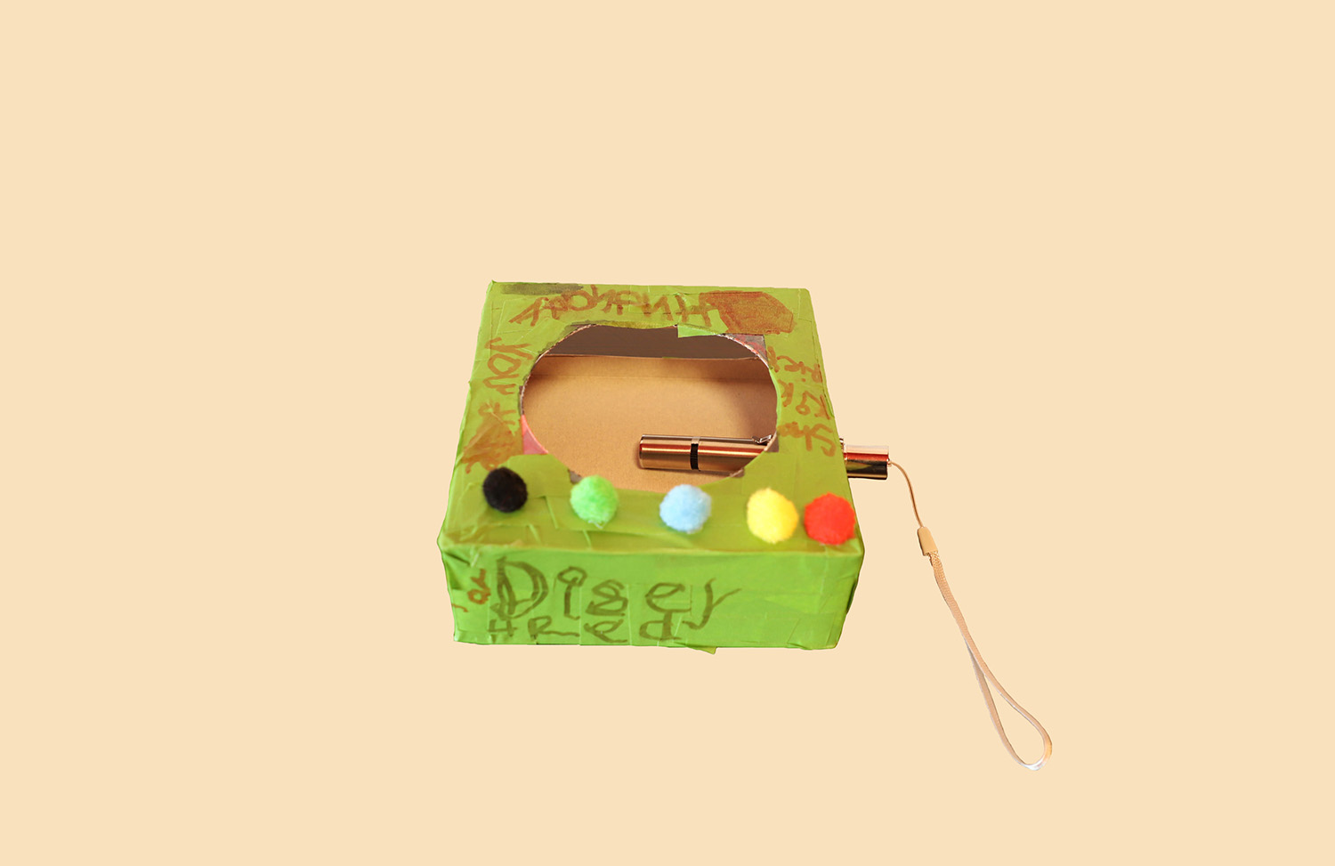 Green cardboard box with a hole cut in the top. A metal tube has been stuck through the side of the box and is visible through the hole. Colourful pompom balls have been stuck to the top.