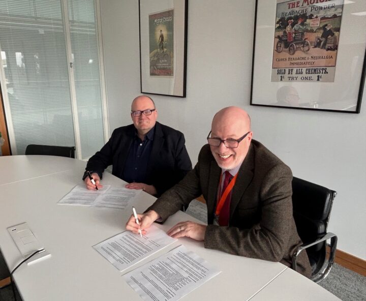 Darren Henley and Jeff James sitting in an office about to sign a document