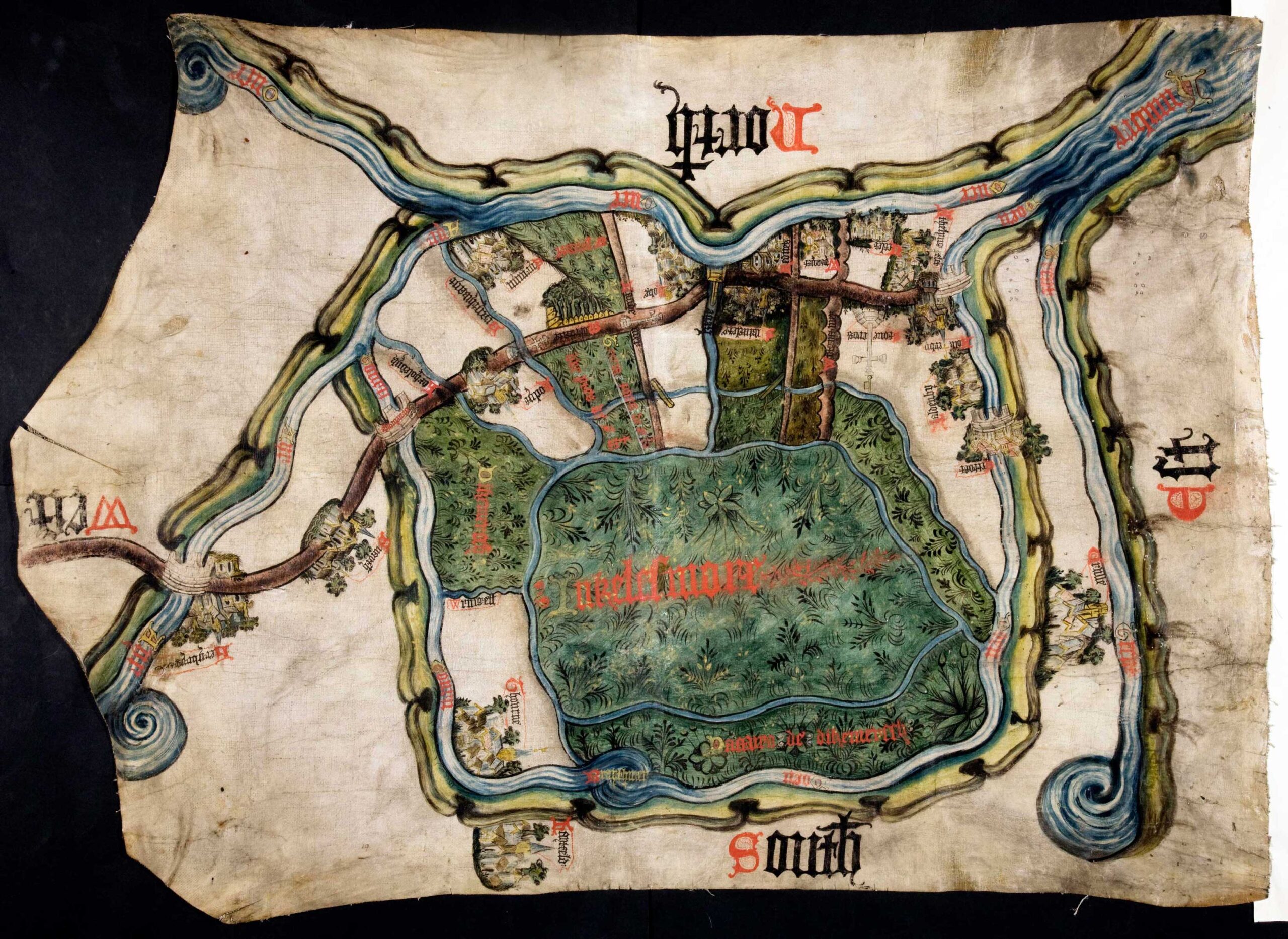 Map painted on parchment. Several fields in the centre are surrounded by rivers on all sides. A road with houses and churches along it goes through the fields and rivers. The words North, South, East and West are written along the sides of the map, indicating the directions.