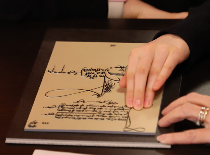 A person uses their hand to feel the raised calligraphy on the tactile John Blanke wage slip.