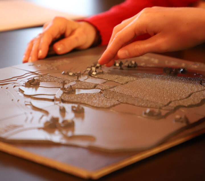 A person using their hand to touch the small houses on the tactile map.