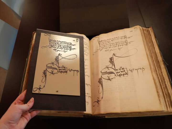 A tactile version of the John Blanke wage slip is held out next to the original document. The tactile version is somewhat smaller but is coloured to look very similar to the original, just with raised lettering.