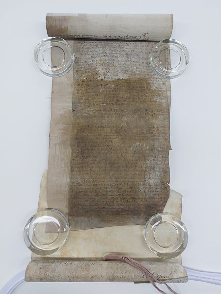 A medieval roll laid out on table. It's handwritten but most of the writing is blocked by a stain.