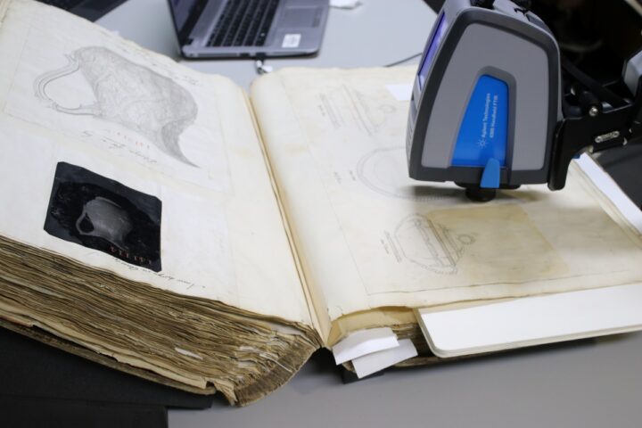 A blue and grey scientific equipment undertaking analysis close to the page of a large, open book.