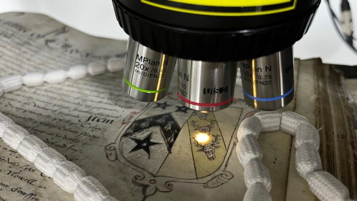 A scientific instrument with three silver heads is shining a small light onto the surface of a document.