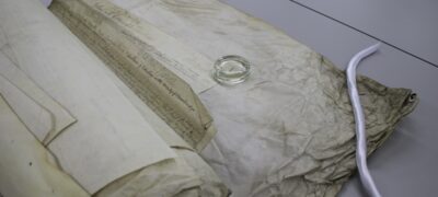 A large paper bundle is partially unrolled on a table. An assortment of weights help hold the different layers down as it's unrolled.
