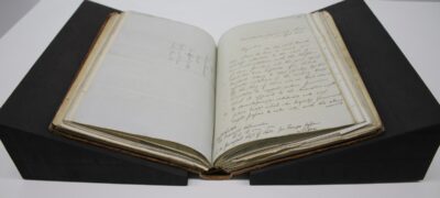A hardback book open on a table, supported by two black, triangular wedges.