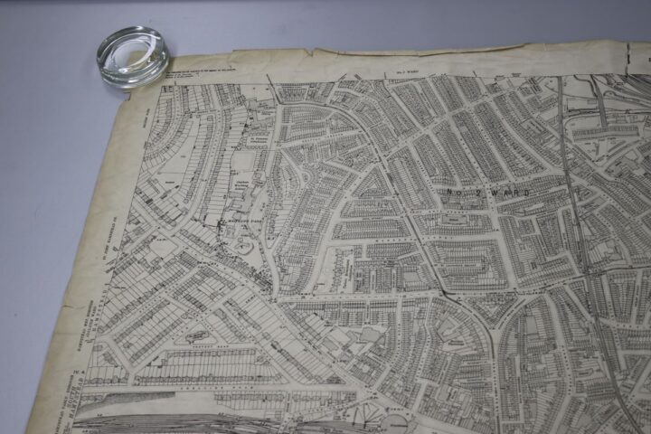 A close up of a large street map on a table. A clear, glass weight holds down the top left corner to keep it lying flat. 